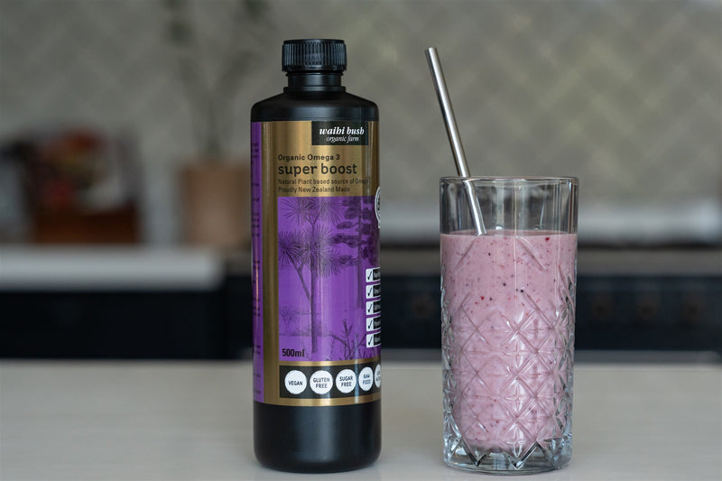 A bottle of Super Boost Omega 3 oil next to a glass filled with a berry smoothie, with a straw in the glass.